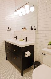 Bright modern bathroom with white subway tile and hexagon floor, sleek black double-sink vanity, matte black faucets, and globe vanity lights.
