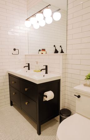Bright modern bathroom with white subway tile and hexagon floor, sleek black double-sink vanity, matte black faucets, and globe vanity lights.