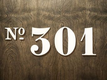 Bold white 'No. 301' sign in decorative font mounted on dark stained wood-grain door plaque