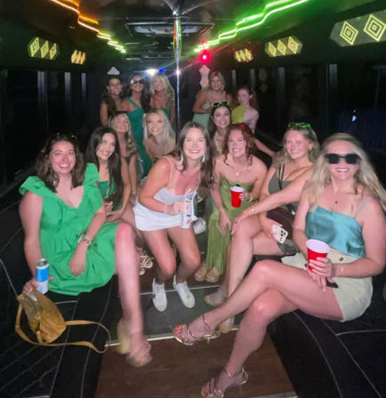 Group of women on a neon-lit party bus, wearing green and white outfits and holding red cups for a fun girls' night out celebration.