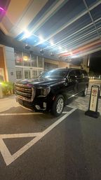 Black GMC SUV parked under a multicolored striped canopy at a hotel drop-off at night, next to a 'No Parking' sign.