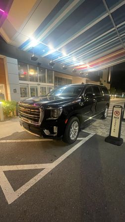 Black GMC SUV parked under a multicolored striped canopy at a hotel drop-off at night, next to a 'No Parking' sign.