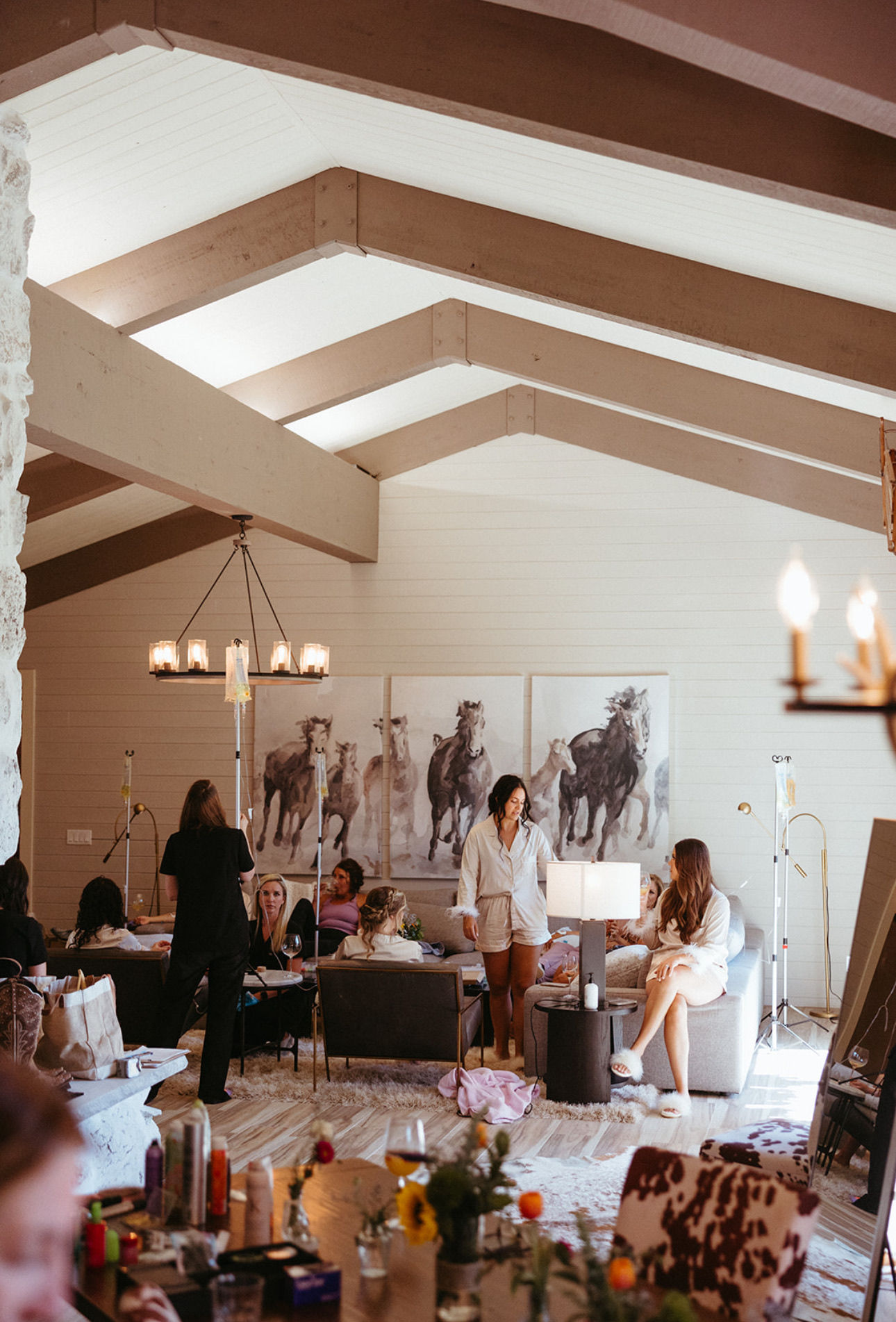 Women in robes enjoying a spa-style pampering party in a modern farmhouse living room with vaulted exposed-beam ceiling, horse paintings and cozy ambient lighting