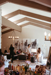 Women in robes enjoying a spa-style pampering party in a modern farmhouse living room with vaulted exposed-beam ceiling, horse paintings and cozy ambient lighting