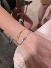 Close-up of a person's wrist wearing two bracelets: a thin gold chain and a silver bangle with a gold bead, casual indoor scene with blurred background