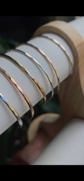 Glinting hammered mixed-metal bangle bracelets in gold and silver neatly stacked on a white leather jewelry display