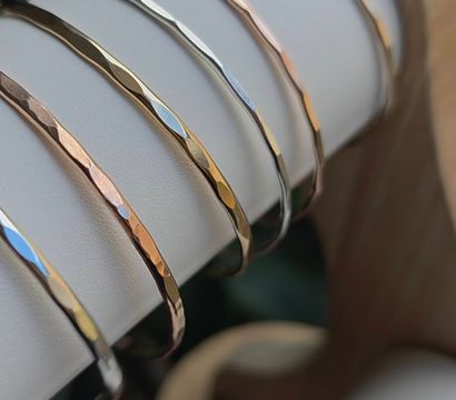 Glinting hammered mixed-metal bangle bracelets in gold and silver neatly stacked on a white leather jewelry display