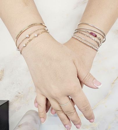 Close-up of hands with French manicure resting on marble, showcasing stacked gold and silver bracelets with pearl and beaded accents and a delicate pavé ring