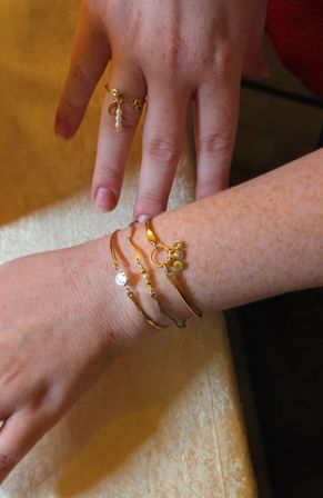 Close-up of a hand with fair, freckled skin wearing stacked gold bracelets and a delicate pearl charm ring