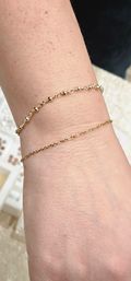 Close-up of a wrist wearing two delicate gold bracelets — a tiny beaded chain and a dainty thin link chain on light skin, minimalist jewelry close-up.