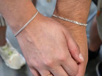 Close-up of two hands wearing matching silver curb-chain bracelets, minimalist couple jewelry and holding hands, stylish & simple accessory detail