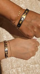 Close-up of two wrists wearing matching silver charm bangles and delicate gold chain bracelets on champagne velvet fabric.