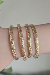 Close-up of four slim engraved gold floral bangles stacked on a wrist — delicate stackable bracelet detail
