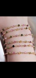 Dainty gold-link stacked bracelets with tiny faceted multicolored gemstone beads (pink, green, yellow) worn on a wrist — boho layering jewelry.