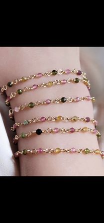 Dainty gold-link stacked bracelets with tiny faceted multicolored gemstone beads (pink, green, yellow) worn on a wrist — boho layering jewelry.