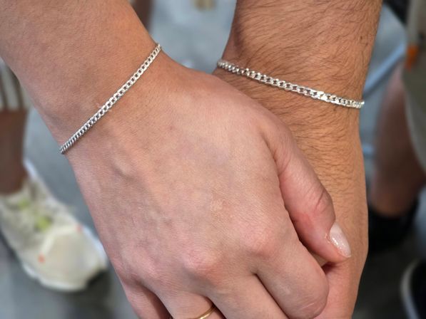 Close-up of two hands wearing matching silver curb-chain bracelets, minimalist couple jewelry and holding hands, stylish & simple accessory detail