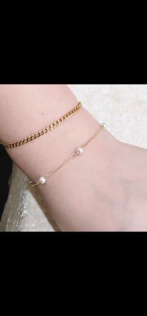 Close-up of ankle wearing two gold anklets — a chunky curb chain and a delicate chain dotted with small white pearls, minimalist jewelry detail.