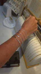 Close-up of an arm wearing stacked delicate gold and silver bracelets — mixed chain links and a slim pavé bangle — held over a jewelry display in a boutique.