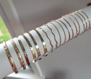 Gleaming gold-tone bangles and textured bracelets arranged on a white cylindrical display near a window