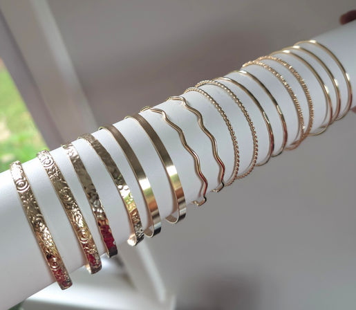 Gleaming gold-tone bangles and textured bracelets arranged on a white cylindrical display near a window