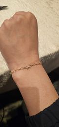 Close-up of a wrist wearing a delicate gold chain bracelet with oval links and a small bow-shaped charm on a soft, neutral background