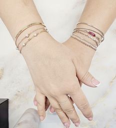 Close-up of hands with French manicure resting on marble, showcasing stacked gold and silver bracelets with pearl and beaded accents and a delicate pavé ring