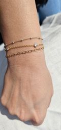 Close-up of a sunlit wrist wearing stacked delicate gold chain bracelets with tiny silver beads and bezel-set crystals — minimalist gold jewelry close-up