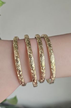 Close-up of four slim engraved gold floral bangles stacked on a wrist — delicate stackable bracelet detail