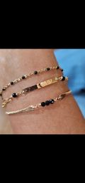 Chic layered gold bracelets on a wrist — hammered bar and delicate chains accented with black faceted beads, close-up jewelry shot.