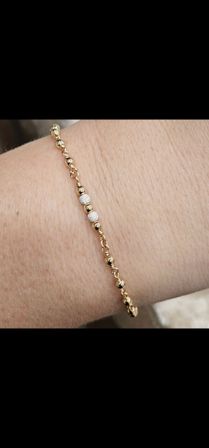 Close-up of a dainty gold bead bracelet with three sparkling textured silver beads worn on a wrist