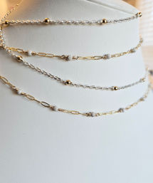 Stacked delicate gold and silver chain necklaces with tiny textured bead accents draped on a white leather jewelry display