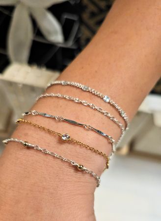 Close-up of stacked delicate silver and gold chain bracelets on a wrist, minimalist jewelry with a bezel-set crystal and textured links