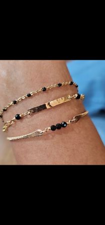 Chic layered gold bracelets on a wrist — hammered bar and delicate chains accented with black faceted beads, close-up jewelry shot.