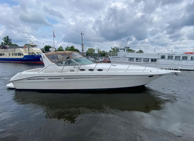 Sleek white cabin cruiser motor yacht moored at a marina under a dramatic cloudy sky, reflected in calm harbor water