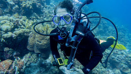 Scuba diver with mask and regulator exploring a vibrant tropical coral reef, yellow fins and rising bubbles visible