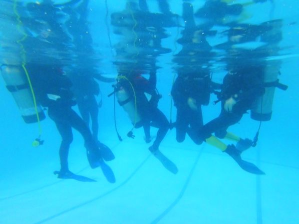 Group of scuba divers training underwater in a clear swimming pool, wearing tanks, wetsuits and fins near the surface