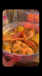 Close-up of a late-night seafood boil in a foil tray with shrimp, crab legs and corn in seasoned broth, colorful bokeh lights in the background.