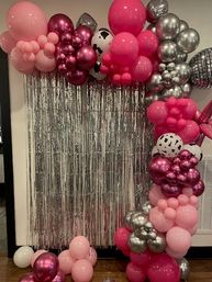 Pink and silver balloon arch with magenta, metallic and cow-print balloons plus disco-ball accents framing a shimmering silver tinsel photo backdrop for an indoor party