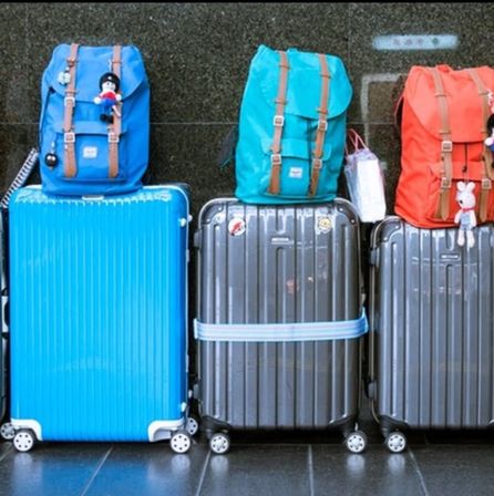 Travel luggage: three hard-shell suitcases with colorful backpacks (blue, teal, red) and small plush keychains lined up on a glossy floor.