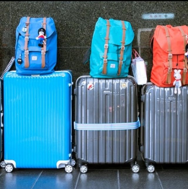 Travel luggage: three hard-shell suitcases with colorful backpacks (blue, teal, red) and small plush keychains lined up on a glossy floor.
