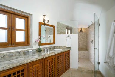 Bright spa-like bathroom with granite countertop, wooden lattice cabinets, wall mirror and orchid beside a frosted wood window, plus a glass-enclosed tiled walk-in shower