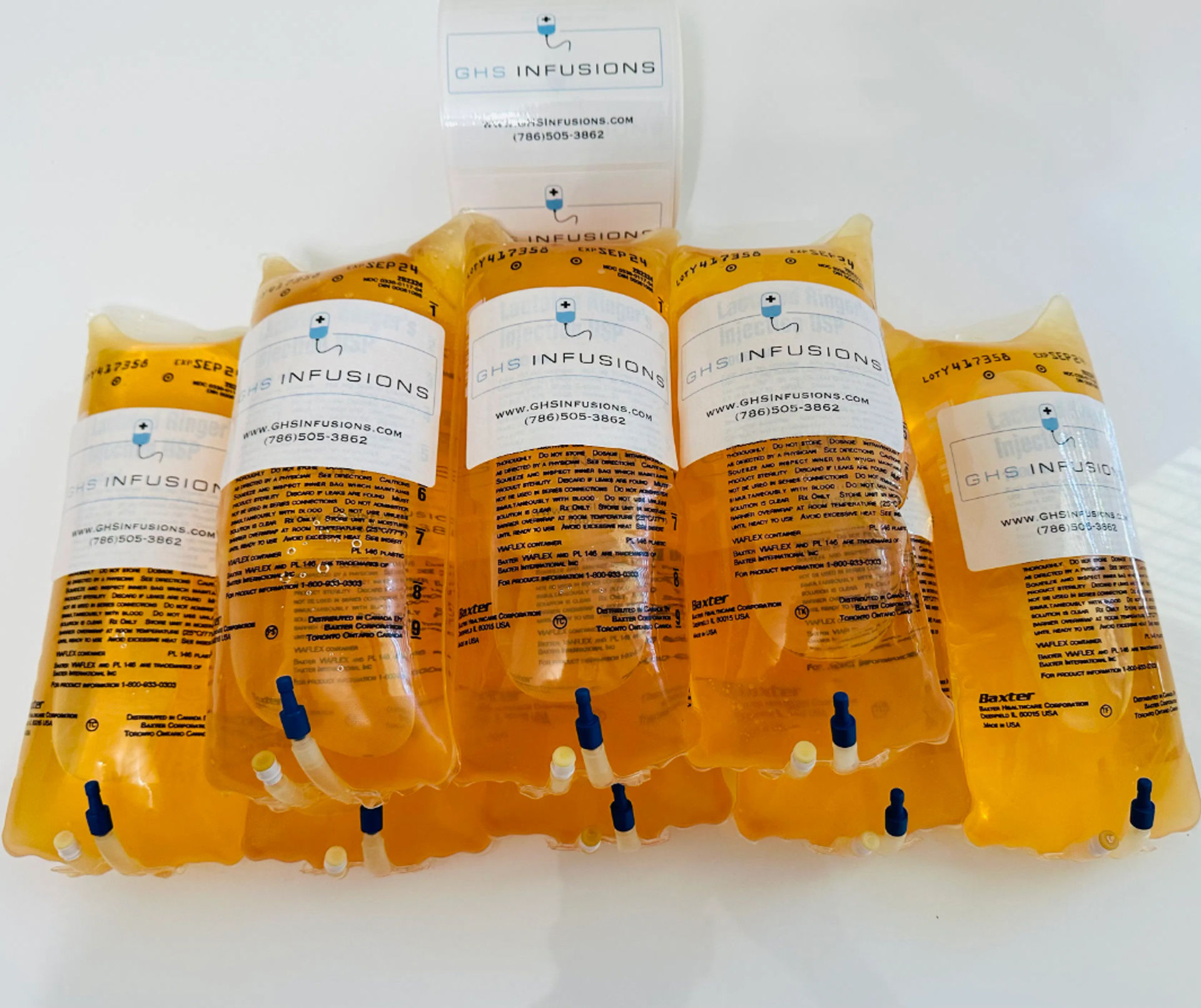 Bright amber IV infusion bags with clear medical labels and blue ports arranged on a white surface — intravenous vitamin drip and hydration therapy supplies.