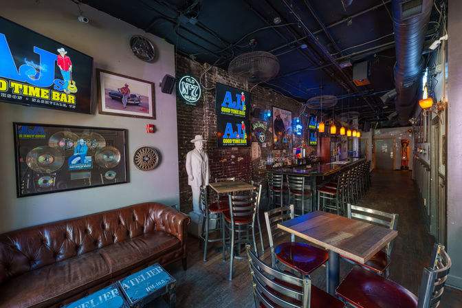 Cozy downtown Nashville bar interior with exposed brick, long wooden bar and high stools, tufted leather sofa, music memorabilia and neon signs, pendant lights and a cowboy mannequin