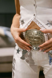 Close-up of hands with long pale-pink nails fastening an ornate silver country-western belt buckle on a white, star-studded, rhinestone-trimmed outfit — Nashville country fashion.
