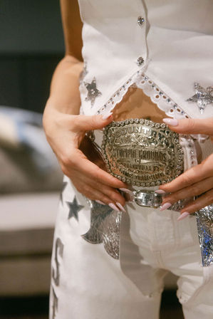 Close-up of hands with long pale-pink nails fastening an ornate silver country-western belt buckle on a white, star-studded, rhinestone-trimmed outfit — Nashville country fashion.