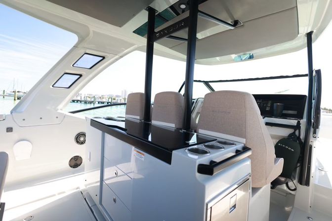 Cockpit of a modern white motorboat with three beige helm seats, glossy black wet-bar countertop with cup holders and drawers, overlooking a sunny marina and calm water—ready for a day on the water.