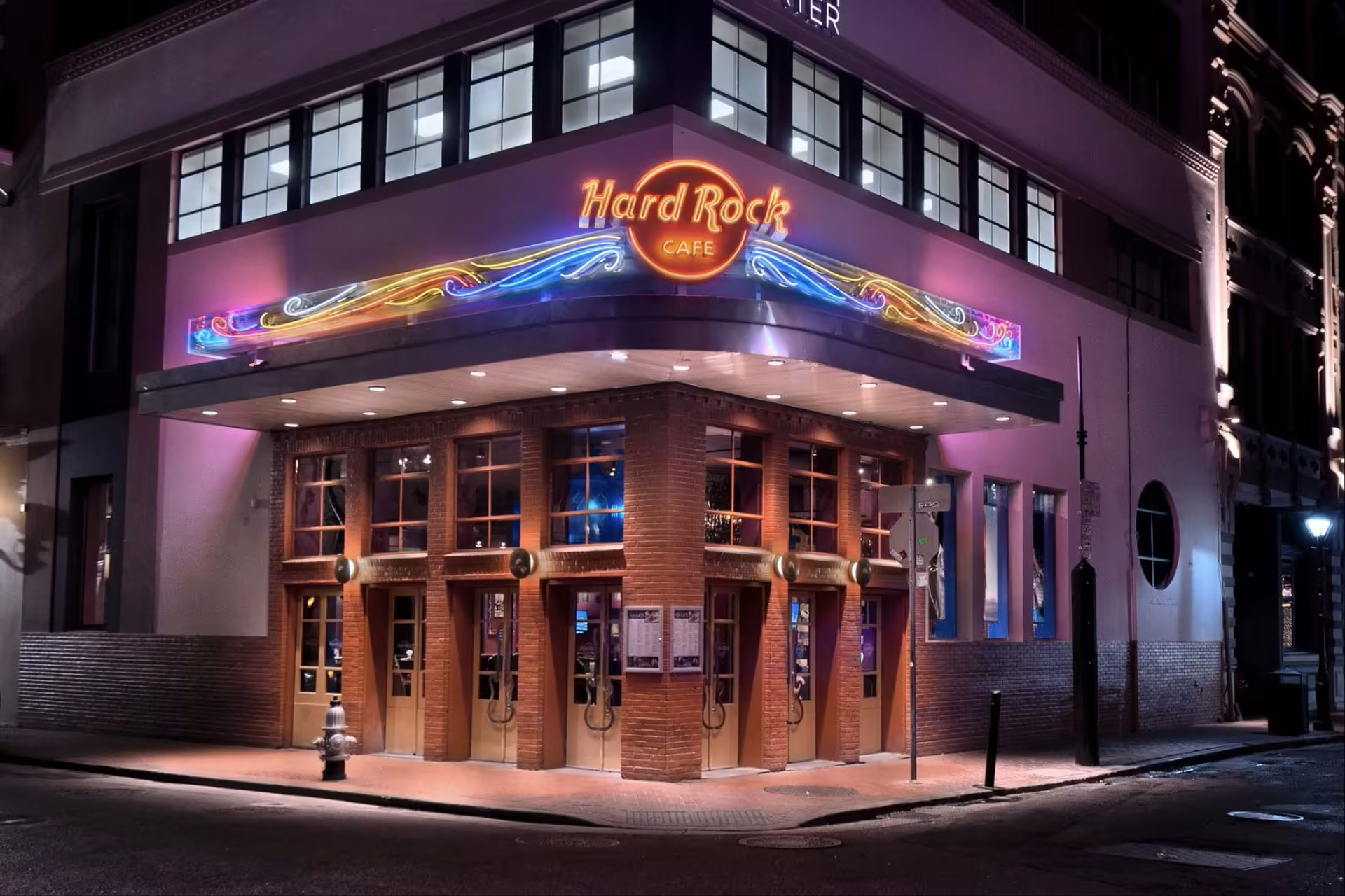 Neon-lit music café on a downtown corner at night with a colorful swirling marquee, brick facade, multiple wooden doors and warm interior glow