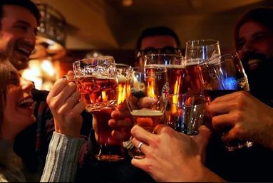 Group of friends clinking pint glasses of amber beer in a cozy pub bar — close-up of hands toasting during a lively night out