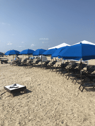 Row of bright blue beach umbrellas and wooden lounge chairs on a sandy beach under a clear blue sky — resort-style setup for a sunny seaside day.