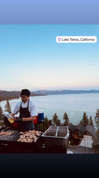 Chef grilling shrimp on an outdoor griddle with Lake Tahoe, California shoreline and mountain lake view at dusk